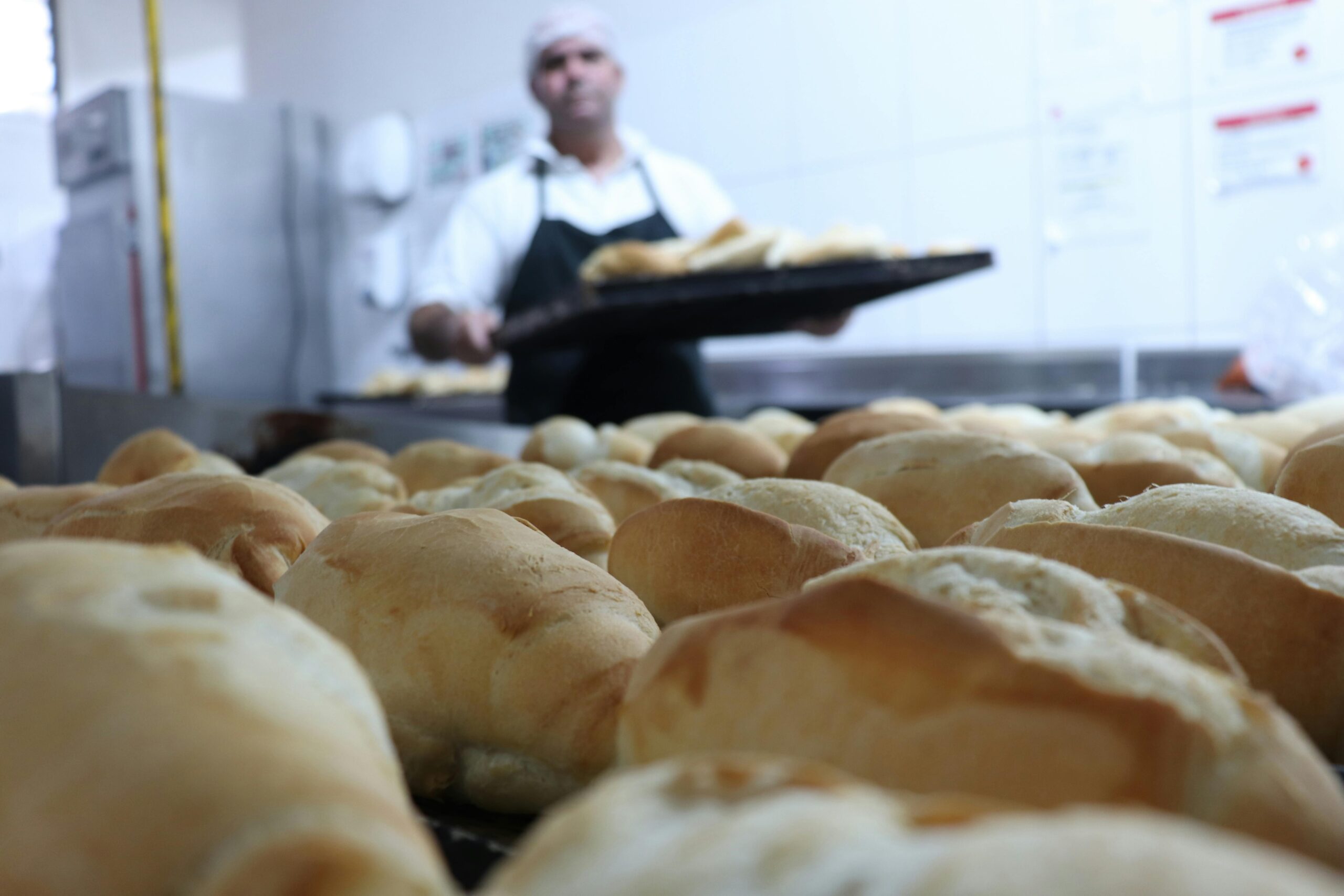 Close-up of freshly baked bread in a bakery kitchen, showcasing golden crusts and a baker in the background.