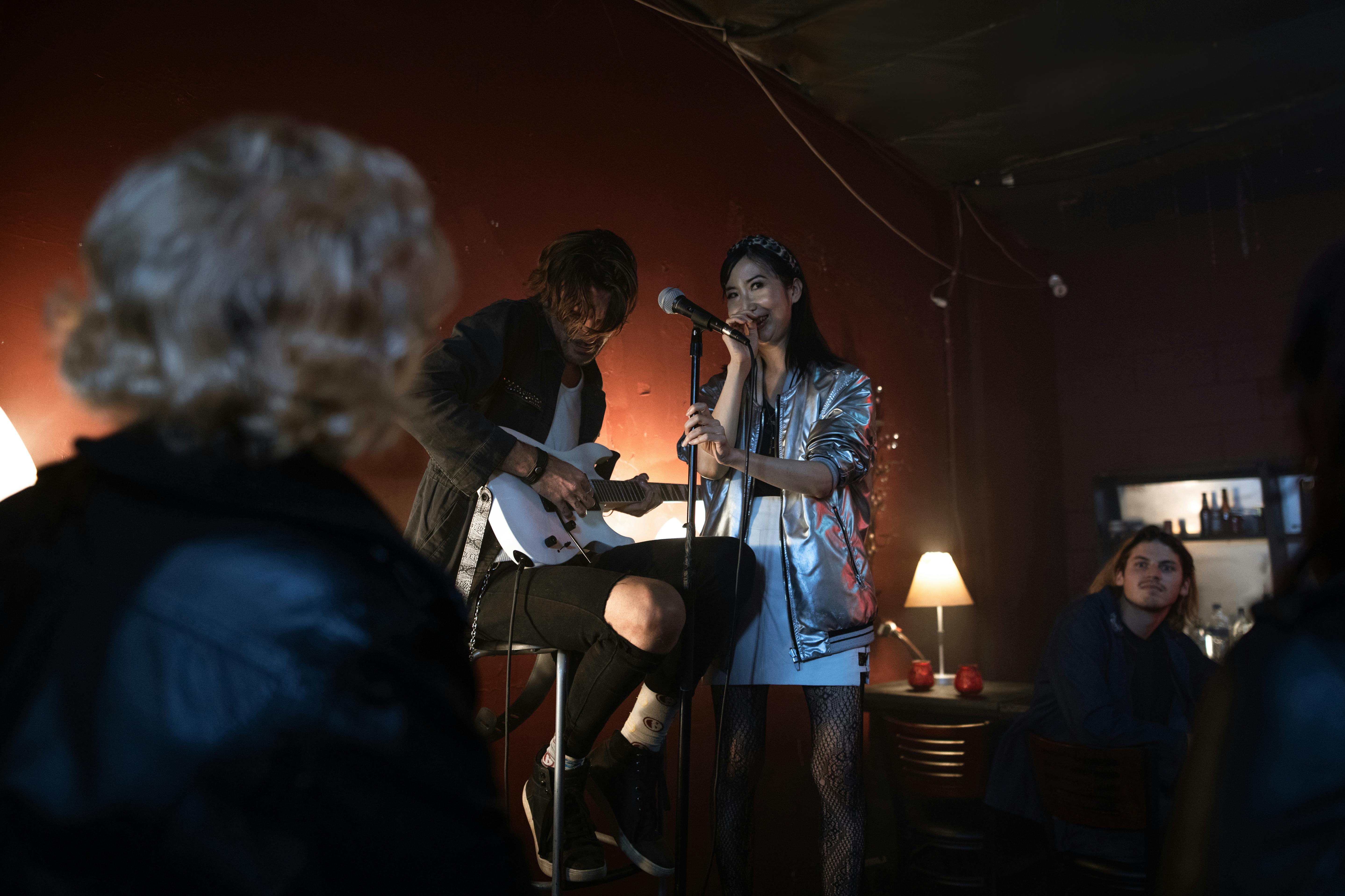 Asian woman sings with guitarist at a cozy bar during a lively night performance.